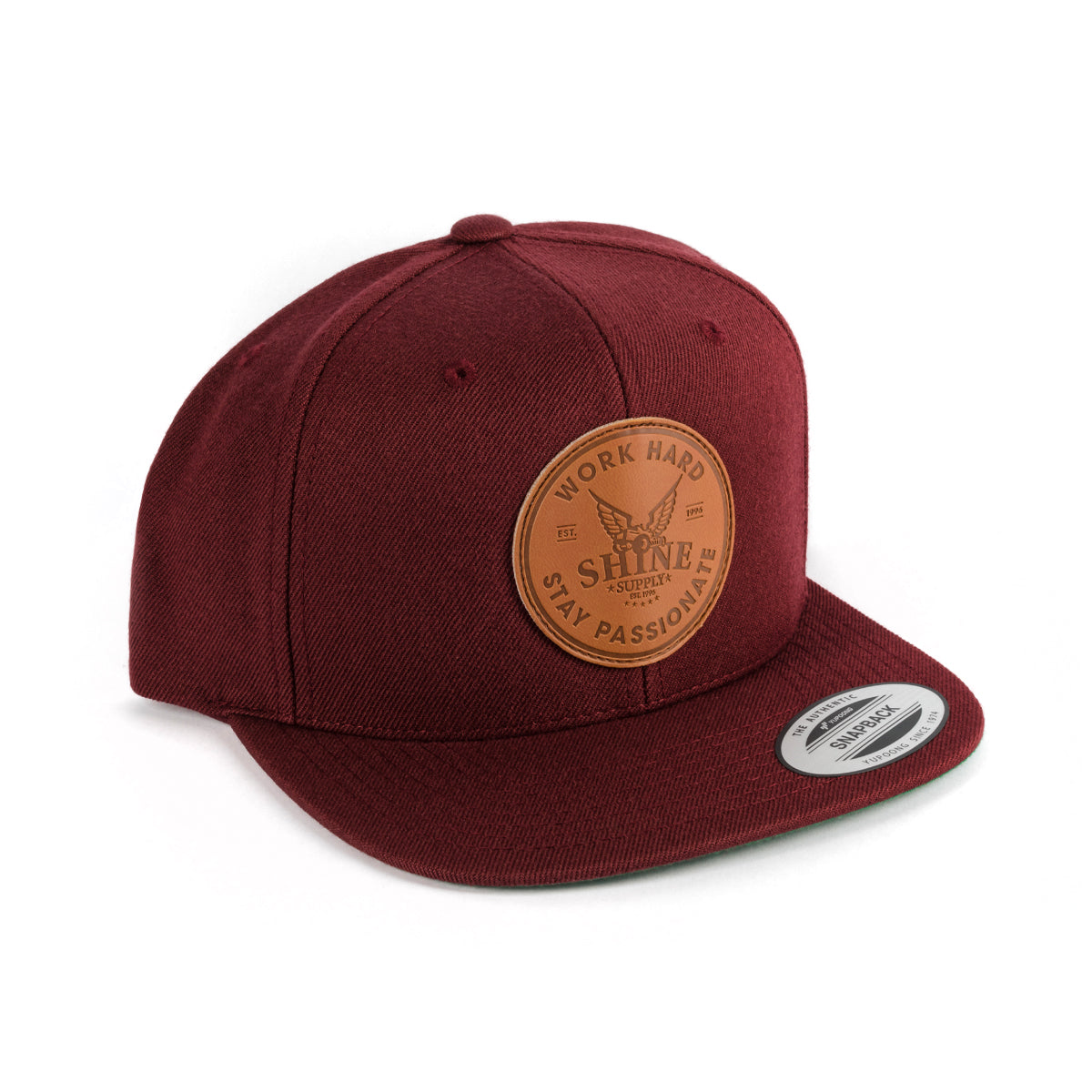 Brick red snapback hat with a leather patch stamped "Work Hard, Shine, Stay Passionate" on the front.