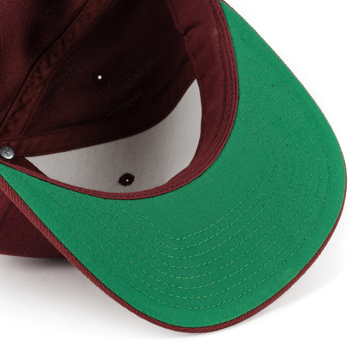 Close-up of a brick red snapback hat with a contrasting green bill and white interior.