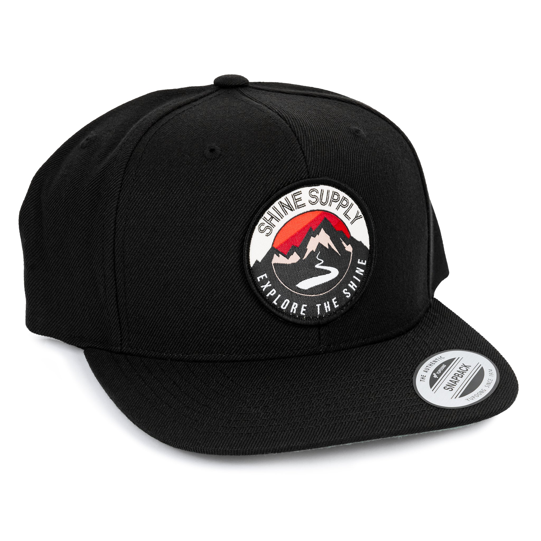 Black snapback hat featuring a round "Shine Supply Explore The Shine" logo with mountain design.