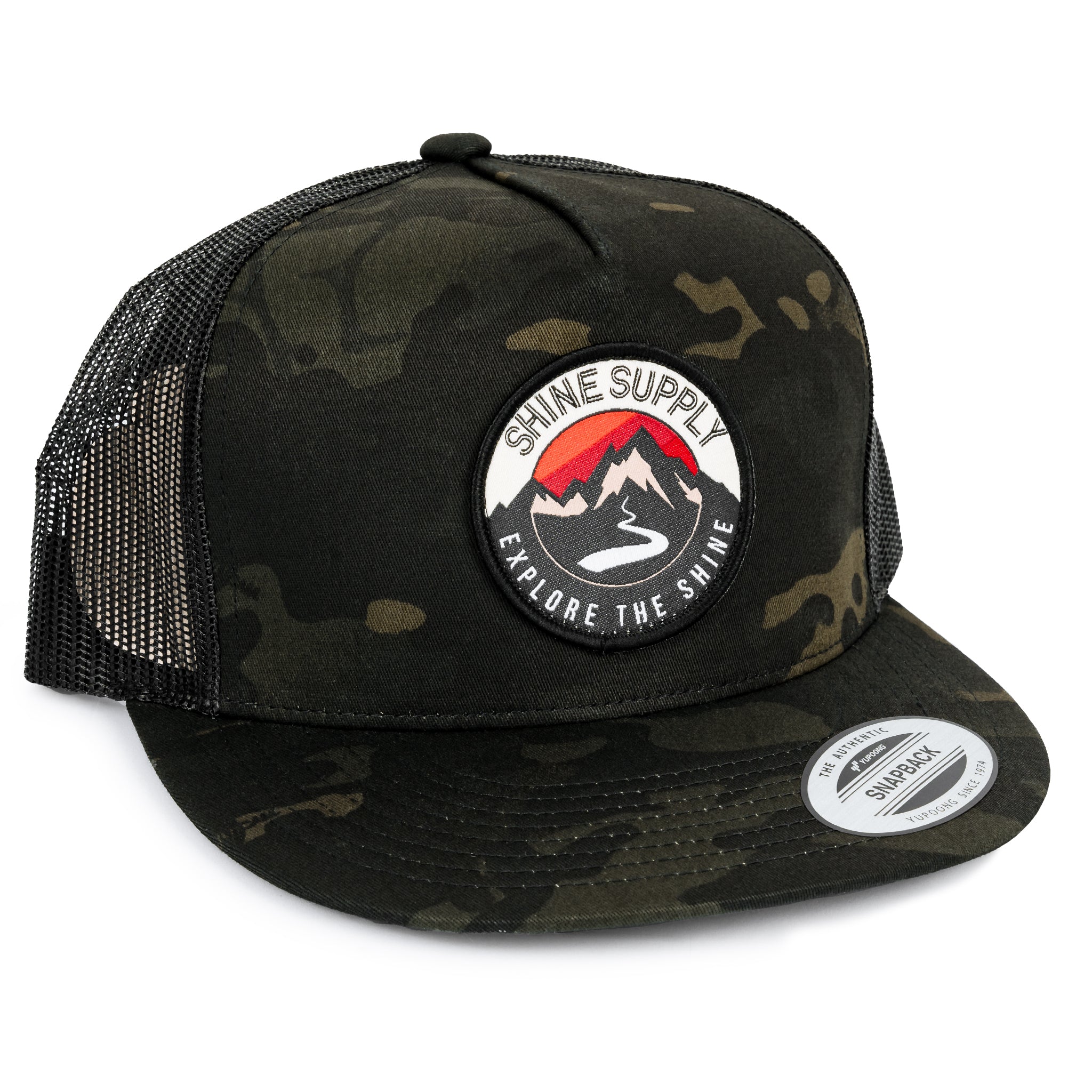 Dark camo trucker snapback hat with mesh back, featuring "Shine Supply Explore the Shine" logo on the front.