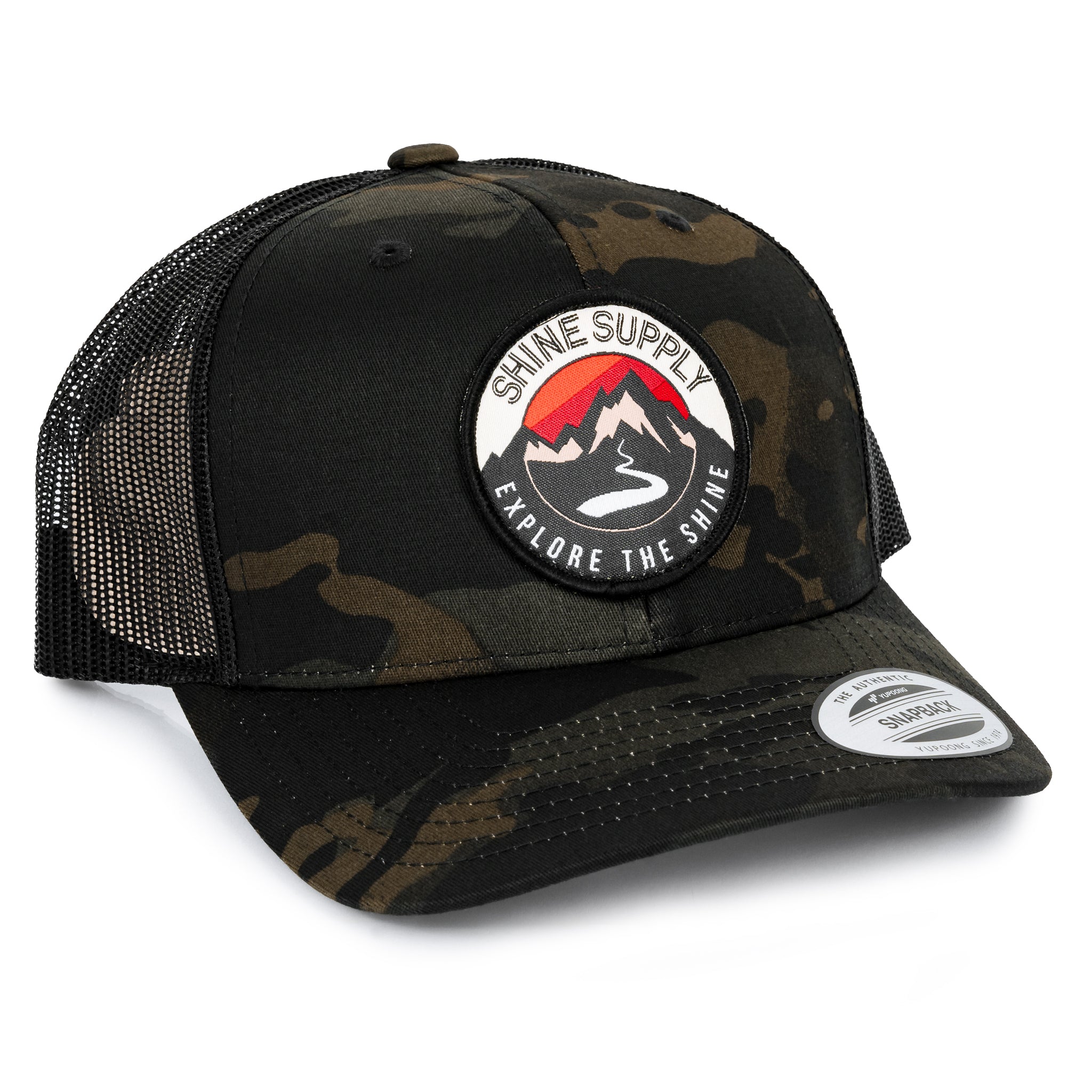 Dark camo trucker snapback hat with curved bill and 'Shine Supply Explore the Shine' patch