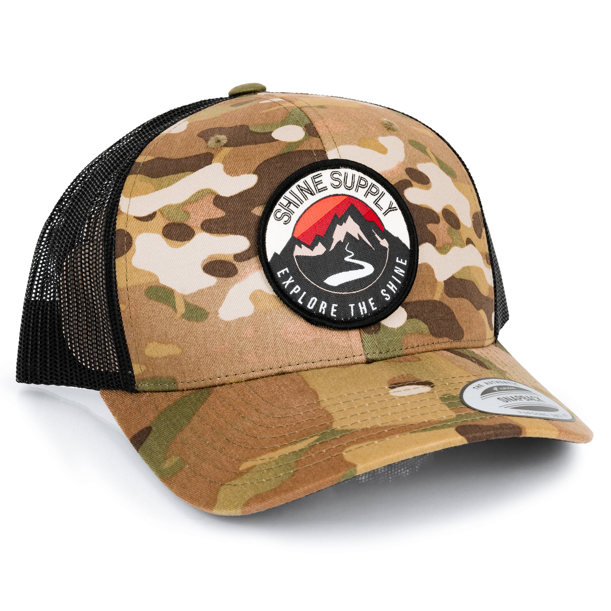 Camo-patterned trucker snapback with curved bill, black mesh back, and "Explore The Shine" logo patch.