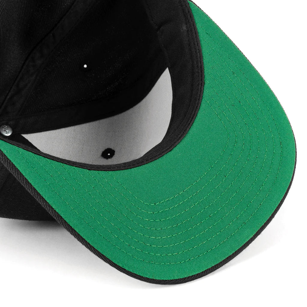 Close-up of a black snapback hat with a green brim and white interior accents.